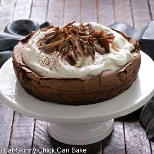 Chocolate Souffle Cake topped with whipped ceam and chocolate shavings on a white cake stand