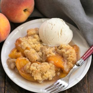Classic Peach Crisp on a white plate with a scoop of vanilla ice cream