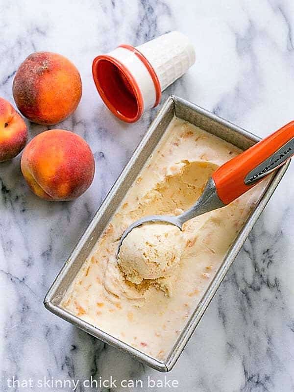 Fresh Peach Ice Cream in a loaf pan with an orange handled ice cream scoop.