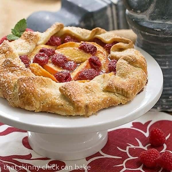 Peach Raspberry Galette on a white ceramic cake stand on a red and white napkin.
