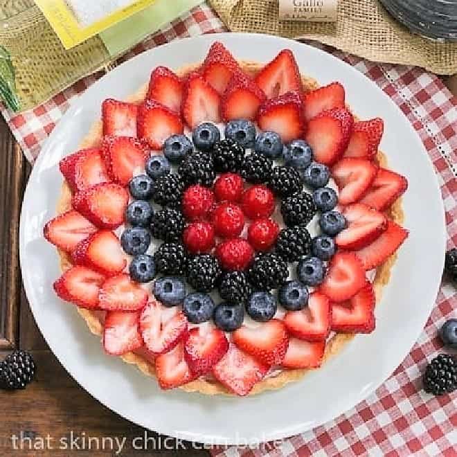 Summer Fruit Tart - Pastry crust with whipped cream and cream cheese filling topped with glorious summer berries Summer Fruit Tart on a white plate with a bottle of white wine.