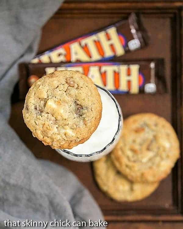 A close up of toffee cookies and toffee bars, one cookie resting on top of a glass of milk.