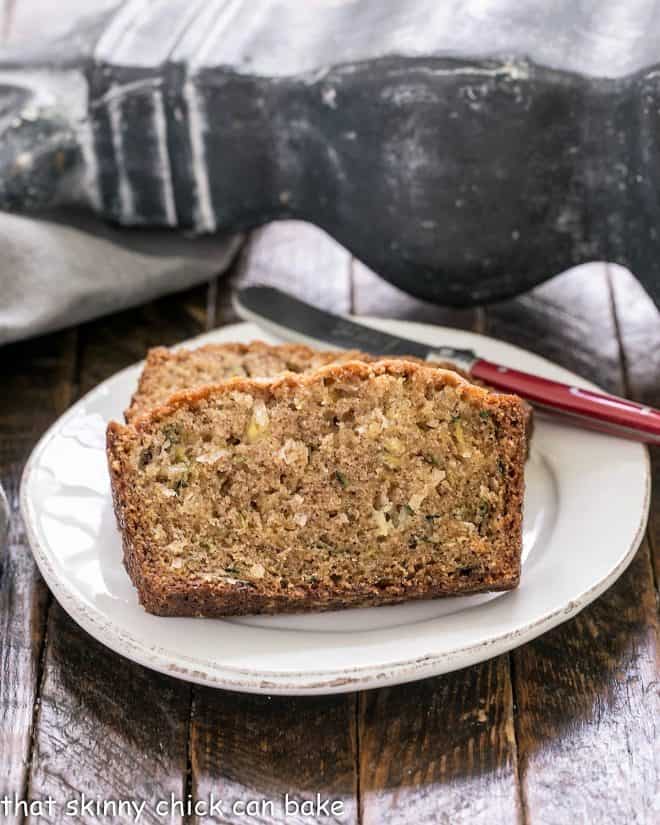 Slices of zucchini bread recipe on a white plate with a red handled knife
