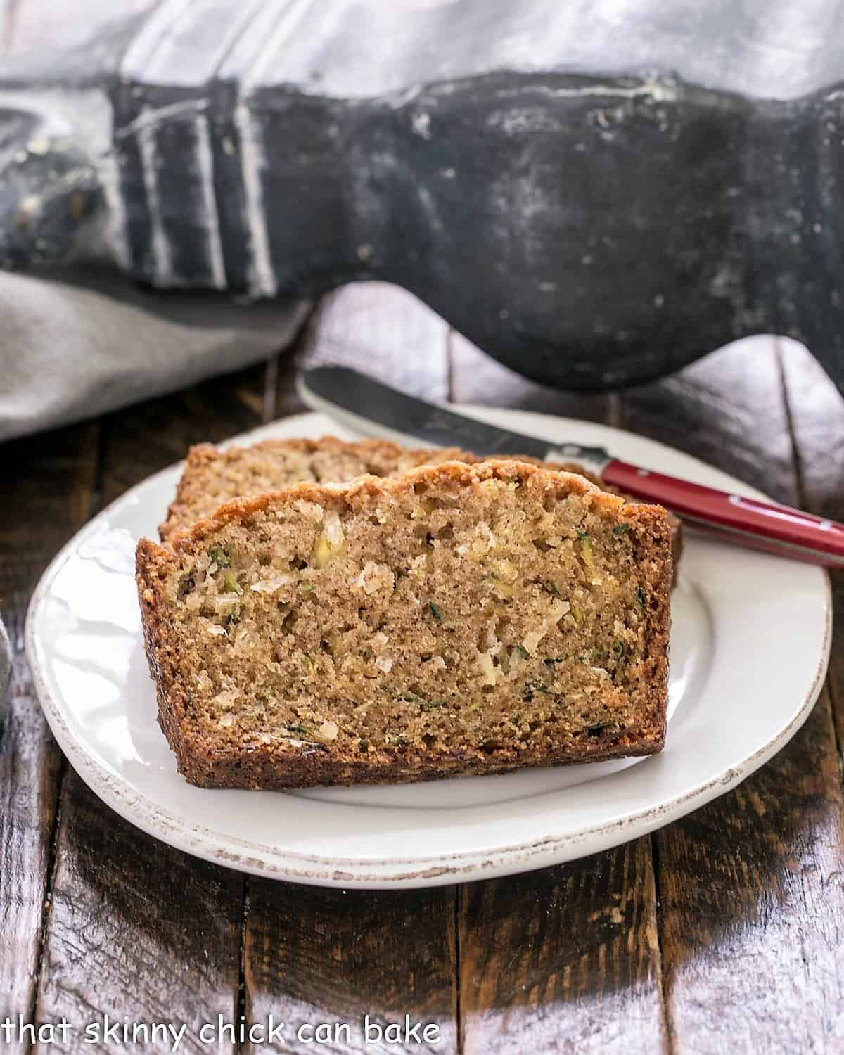 Slices of zucchini bread recipe on a white plate with a red handled knife.