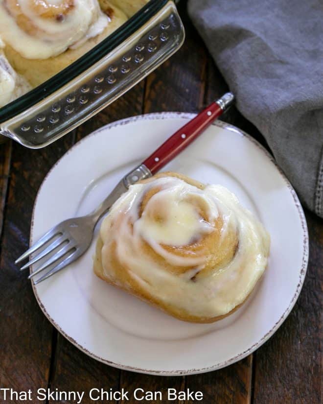 Overhead view of one cinnamon roll on a round white plate with a red handle fork