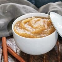 Bowl of homemade cinnamon applesauce next to 2 cinnamon sticks.