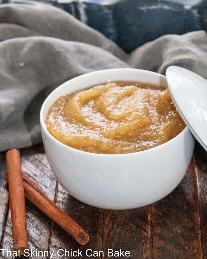 Bowl of homemade cinnamon applesauce next to 2 cinnamon sticks.