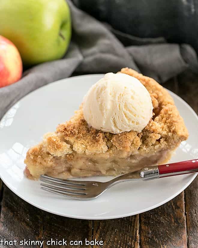 Slice of Dutch Apple Pie topped with a scoop of ice cream on a white dessert plate.