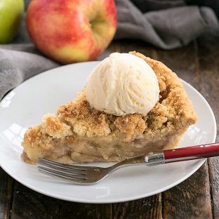 Slice of the best apple pie recipe topped with ice cream on a white plate