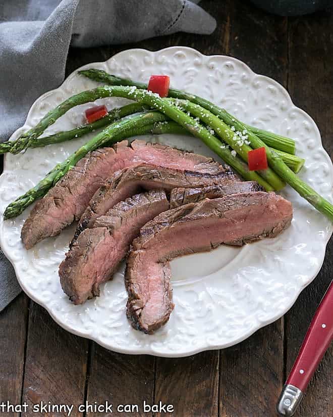 Easy Grilled Flank Steak slices on a white dinner plate with aspargus.