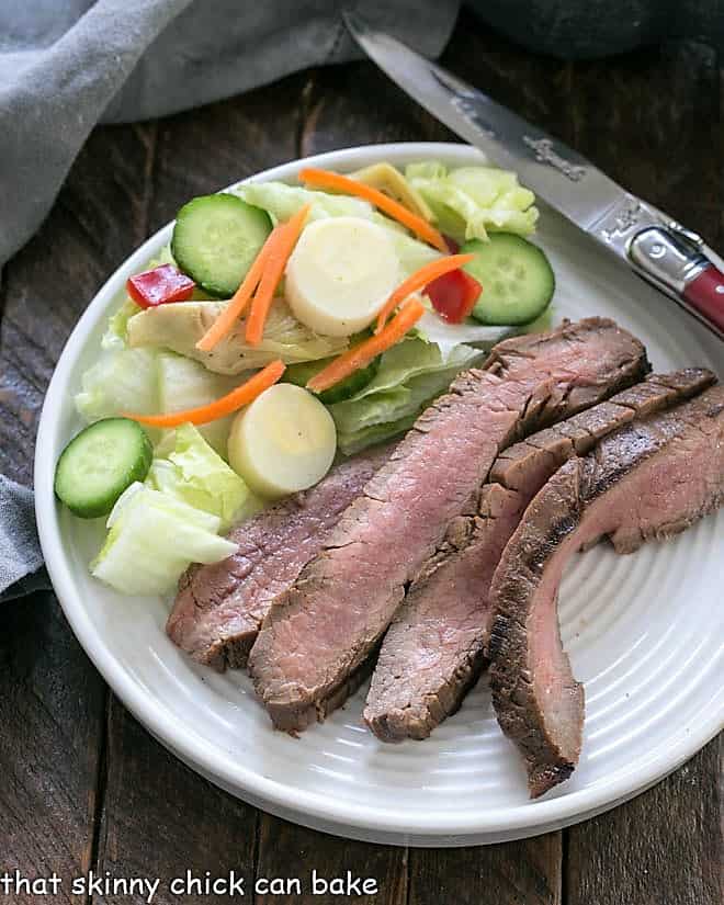 Overhead view of Easy Grilled Flank Steak on a dinner plate with a green salad.