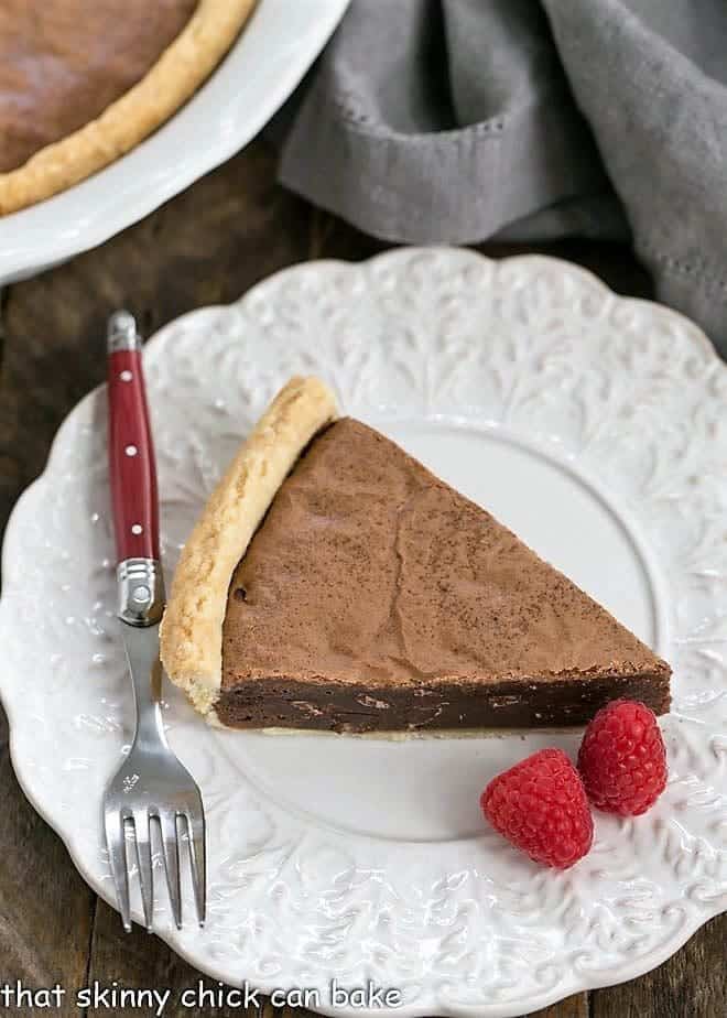 Fudgy Brownie Pie - Rich brownie filling studded with chocolate chips and baked in a flaky pastry shell! Fudgy Brownie Pie on a fancy white plate with raspberries and a red handled fork