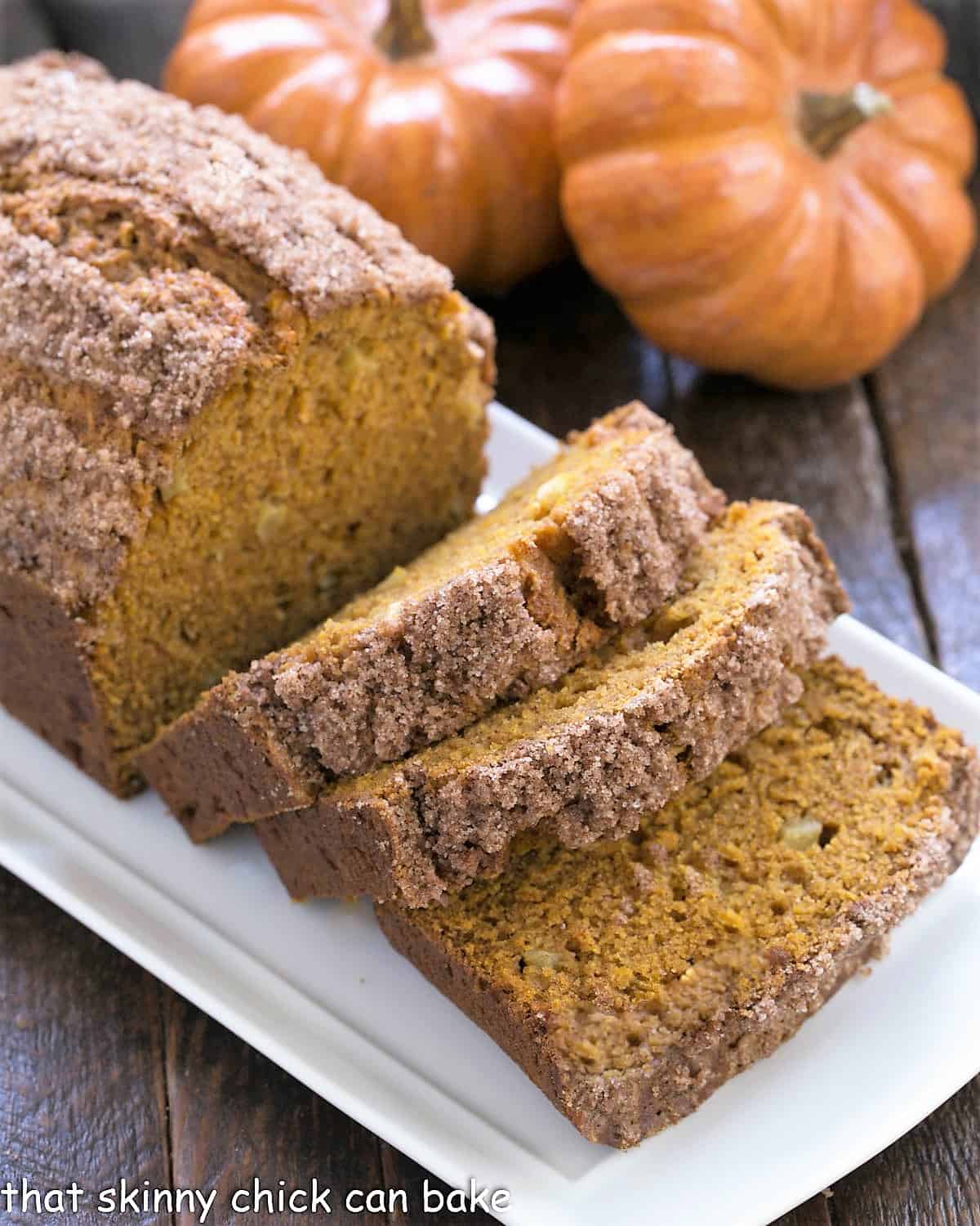 Pumpkin Bread with Apples sliced on a white ceramic tray with 2 mini pumpkins.