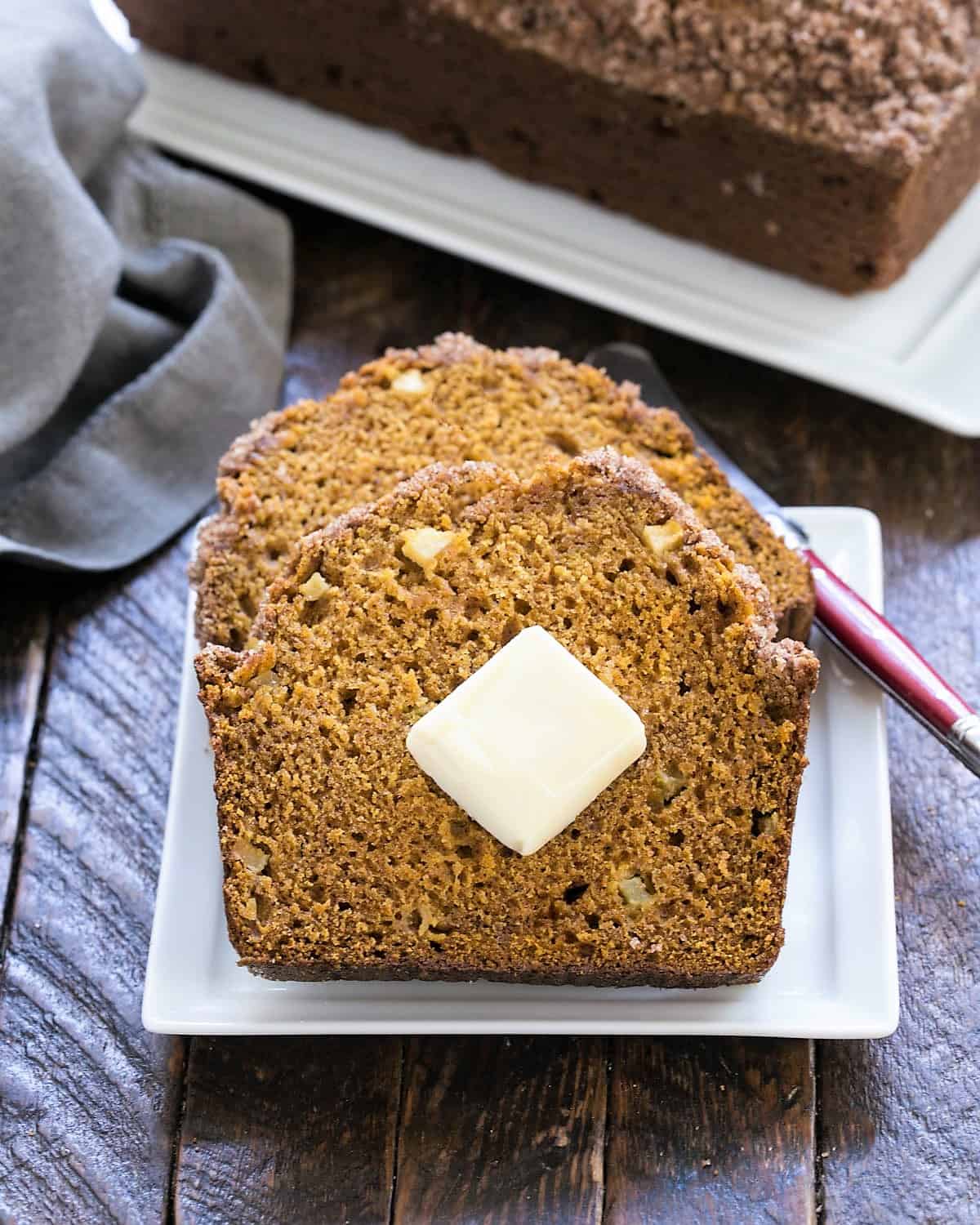 2 slices of an easy pumpkin bread on a white plate in front of a loaf of pumpkin bread on a tray.