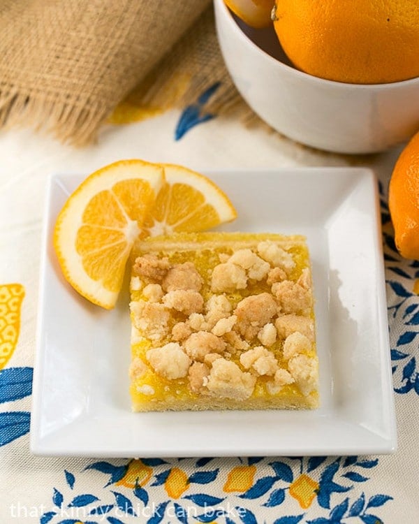 Scrumptious lemon bars with a sugar cookie crumble topping and Meyer lemon filling on a shortbread crust! Meyer Lemon Streusel Bars on a white dish garnished with lemon slices.