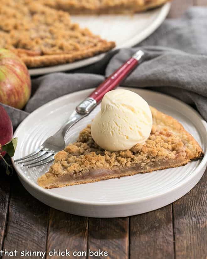 Apple Pie Pizza slice with a scoop of ice cream on a white dessert plate with a red handled fork in front of whole pizza