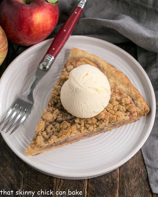 A slice of apple pie pizza on a white plate topped with a scoop of ice cream.