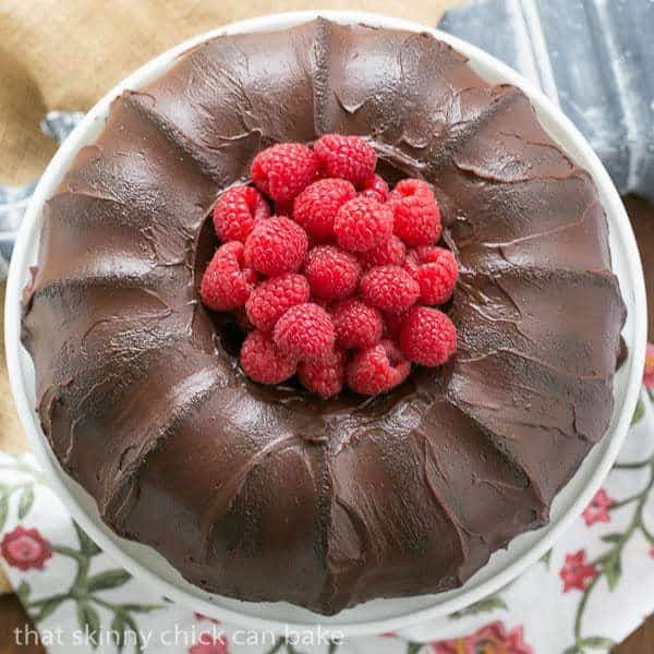 Chocolate Buttermilk Bundt Cake on a white cake stand garnished with fresh raspberries.