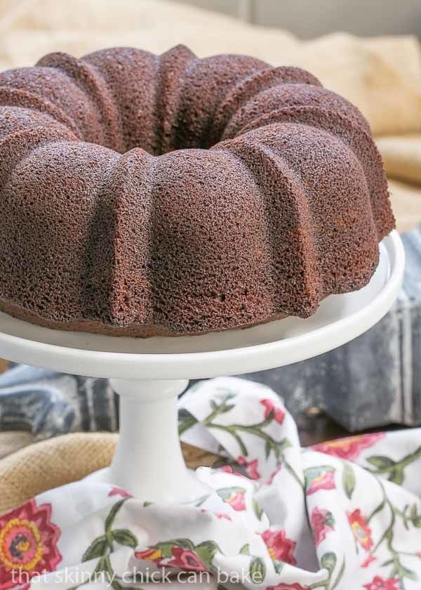 Chocolate Buttermilk Bundt Cake on a white ceramic cake stand with a floral napkin.