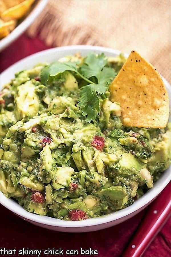  Guacamole in a white serving bowl with cilantro and a tortilla chip.