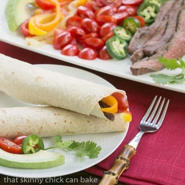 Flank Steak Fajitas - Marinated and grilled beef wrapped in a tortilla for an easy weeknight supper Two Flank Steak Fajitas on a white dinner plate.