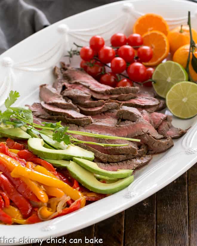 Flank Steak Fajitas and toppings on a white platter.