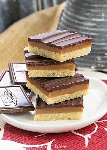 Ganache Topped Caramel Bars stacked high on a white plate over a red and white napkin