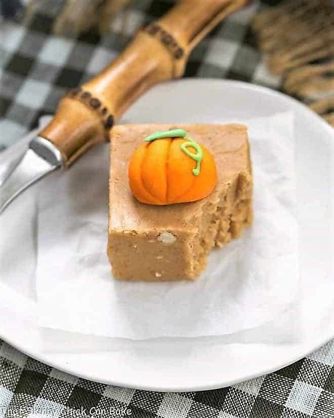 Easy Pumpkin Fudge on a white plate, topped with a candy pumpkin with a forkful removed
