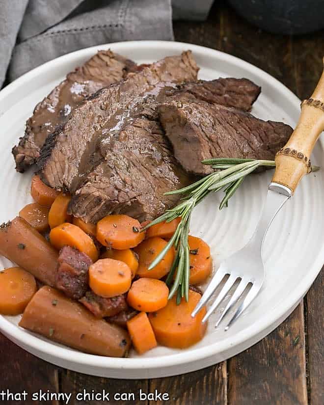 Rosemary Garlic Brisket slices on a white plate with a bamboo fork.