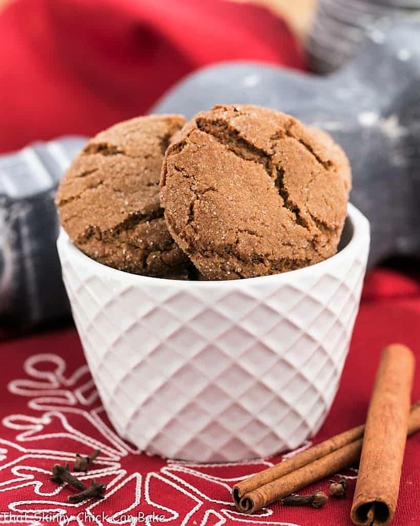 Chewy gingersnaps in a white bowl with cinnamon sticks and cloves.