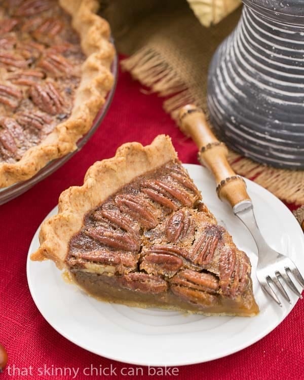 Classic Pecan Pie, with a boozy twist on a white dessert plate with a bamboo handled fork.