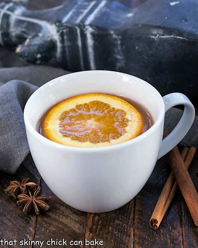 Hot Apple Cider Recipe flavored with vanilla, oranges and warm autumn spices. Perfect for holiday parties, apres ski parties or anytime you need to warm your soul Mulled Apple Cider topped with an orange slice in a round mug.
