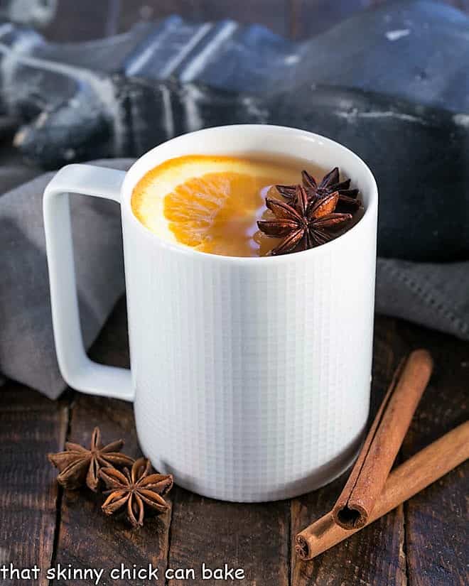 Hot apple cider in a white mug a slice of orange to garnish