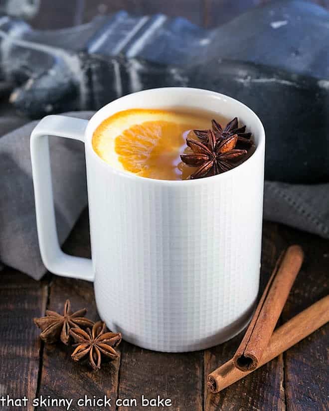 Mulled Apple Cider - Hot cider flavored with vanilla, oranges and warm autumn spices. Perfect for holiday parties, apres ski parties or anytime you need to warm your soul Hot apple cider in a white mug a slice of orange to garnish