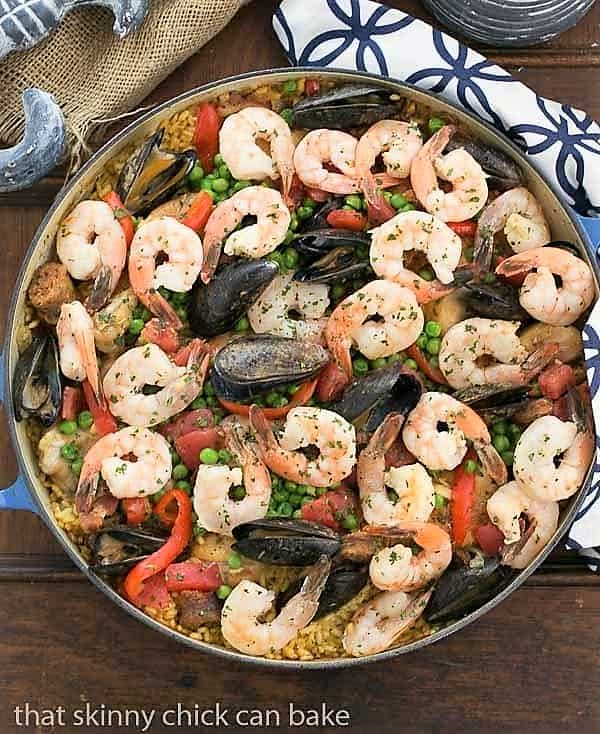 Overhead view of Paella a l'Americaine in a blue cast iron pan on a blue and white patterned napkin.