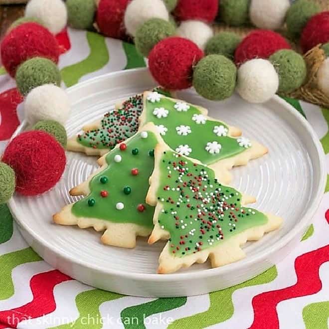 Frosted, sprinkled Christmas sugar cookies on a round white plate.