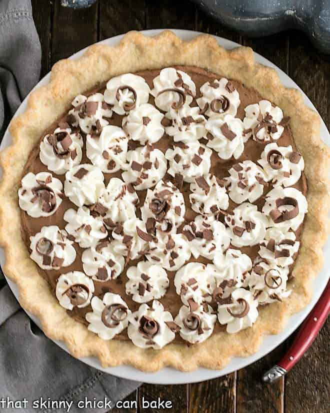 Overhead view of a French Silk Pie in a red ceramic pie plate with whipped cream and chocolate garnishes.