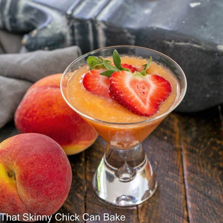 A peach bellini recipe topped with sliced strawberries next to 2 fresh peaches