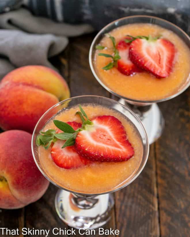 Overhead view of 2 bellinis topped with strawberries next to 2 fresh peaches.