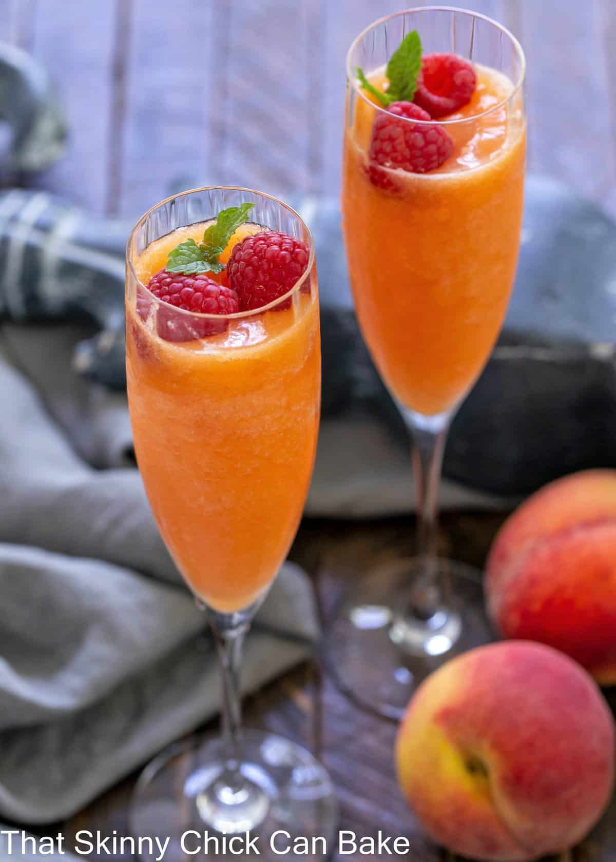 2 bellinis in stemmed champagne glasses topped with fresh raspberries and mint.