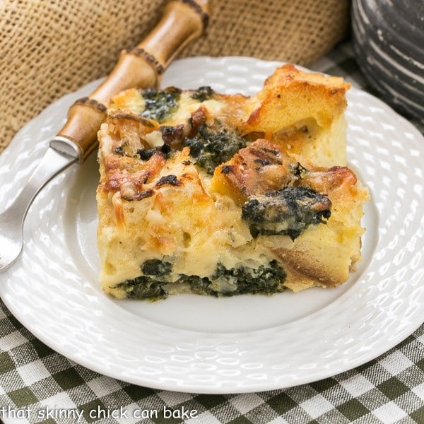 Gruyere Spinach Strata slice on a white plate with a bamboo handle fork.