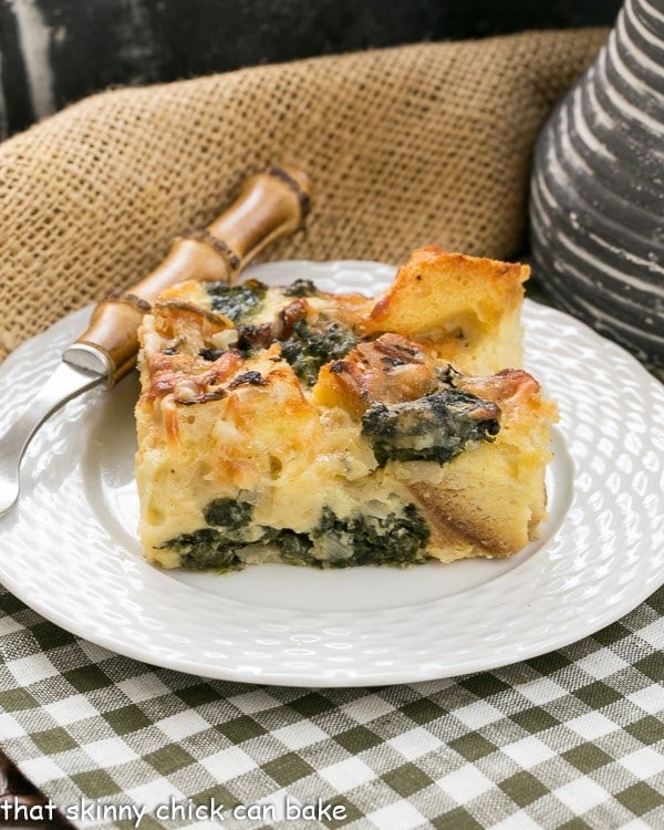 A square of spinach egg casserole on a small white plate on a green and white checked napkin.