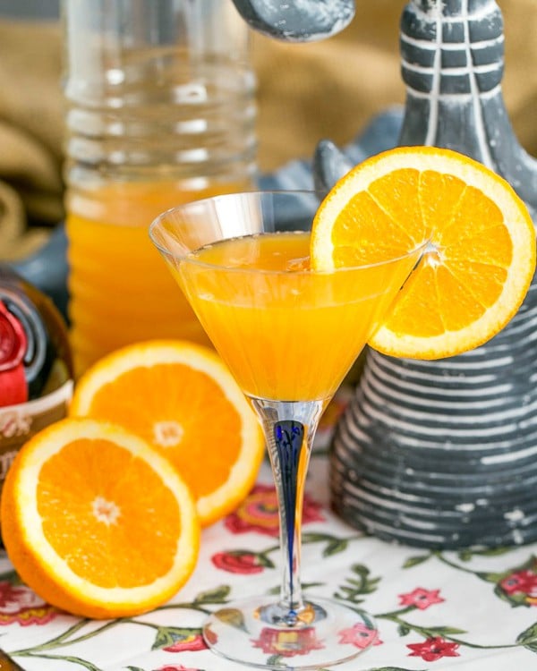 Grand Marnier Mimosas in a glass pitcher with a glass garnished with an orange slice and orange halves in the foreground