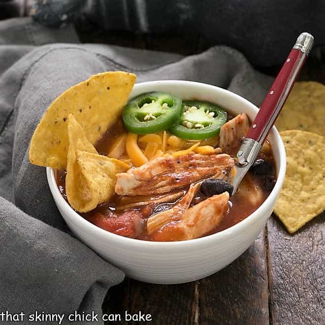 Enchilada soup in a white bowl with tortilla chips to garnish and a red handle spoon