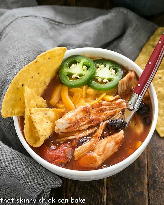 Slow Cooker Chicken Enchilada Soup in a white ceramic bowl garnished with chips and cheese.