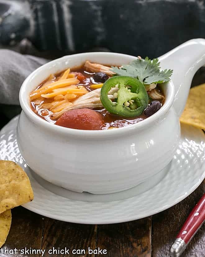 Enchilada Soup in a white crock with chips and a red handle spoon