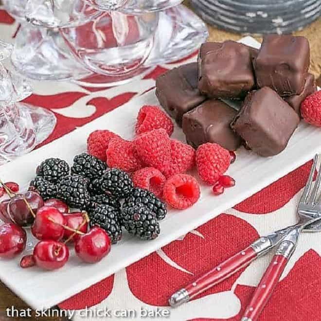 Chocolate Dipped Cheesecake Bites on a white tray with fruit