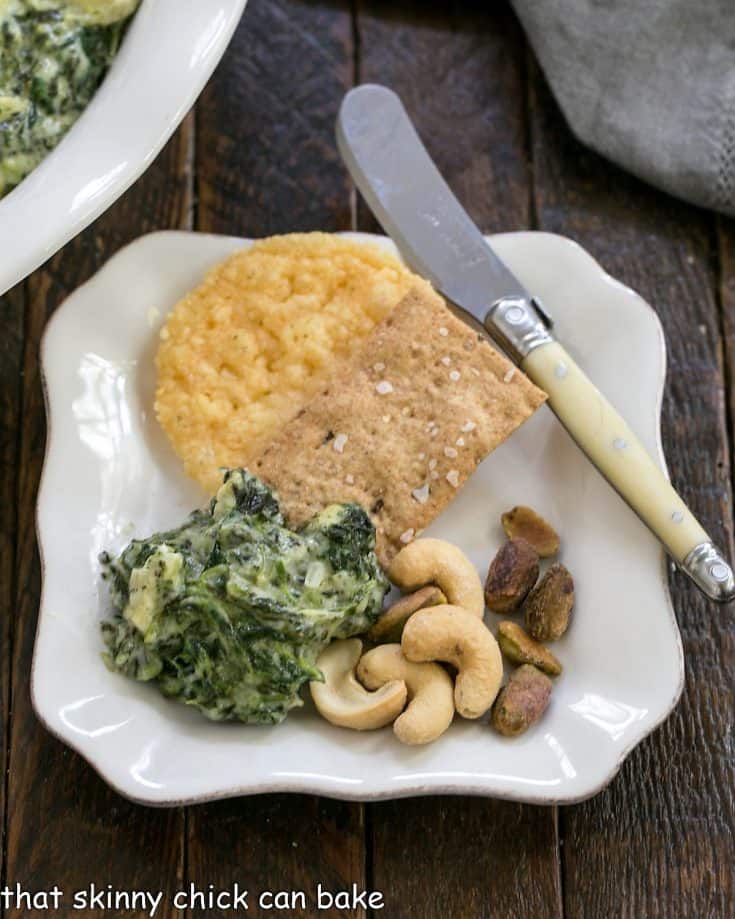 Spinach and artichoke dip on an appetizer plate with crackers and nuts