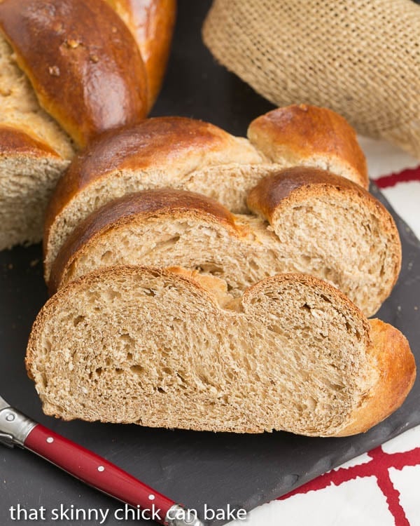 3 slices of Whole Wheat Challah on a slate tray with a red handled butter knife