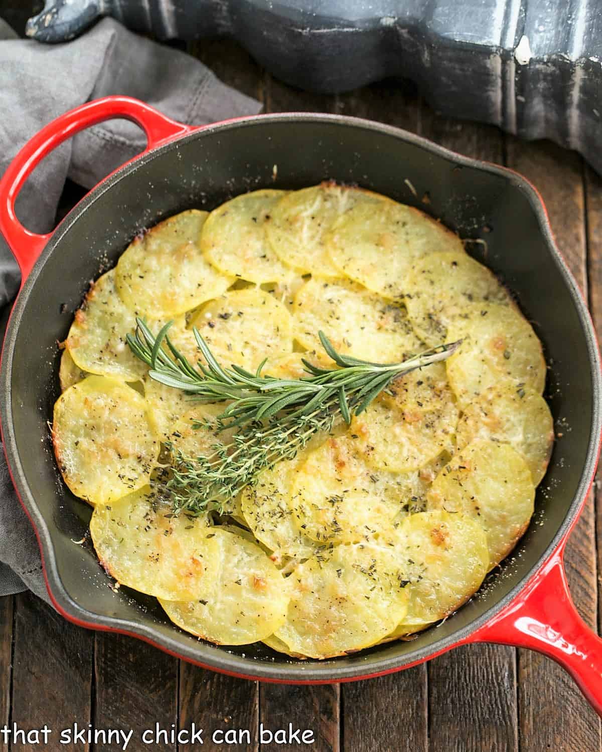 Overhead view of a cooked potato galette in a red ceramic skillet with an herb garnish.